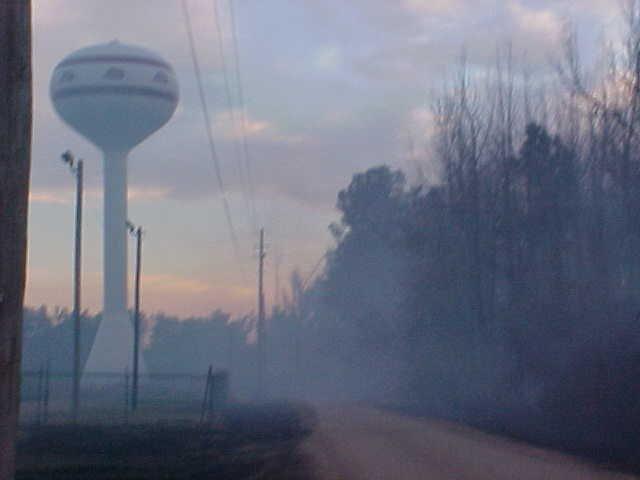 Smoke rises in front of a water tower.